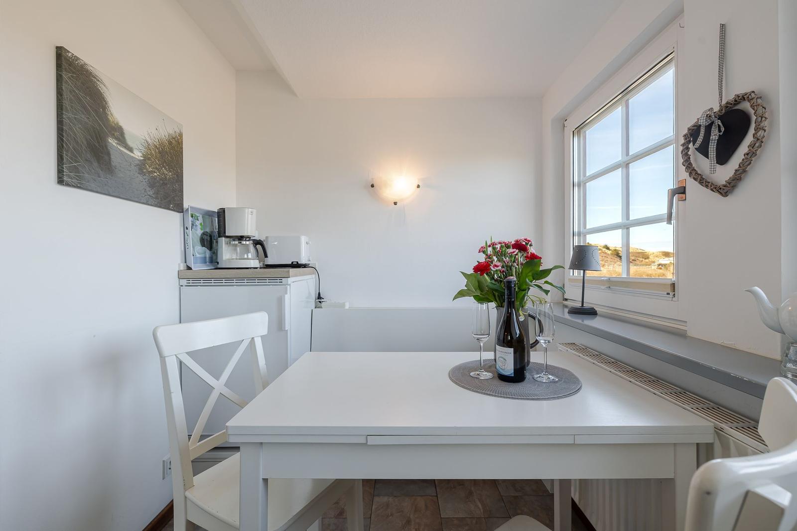 Weißer Tisch mit Stühlen, Fenster, Blumen und Getränke.