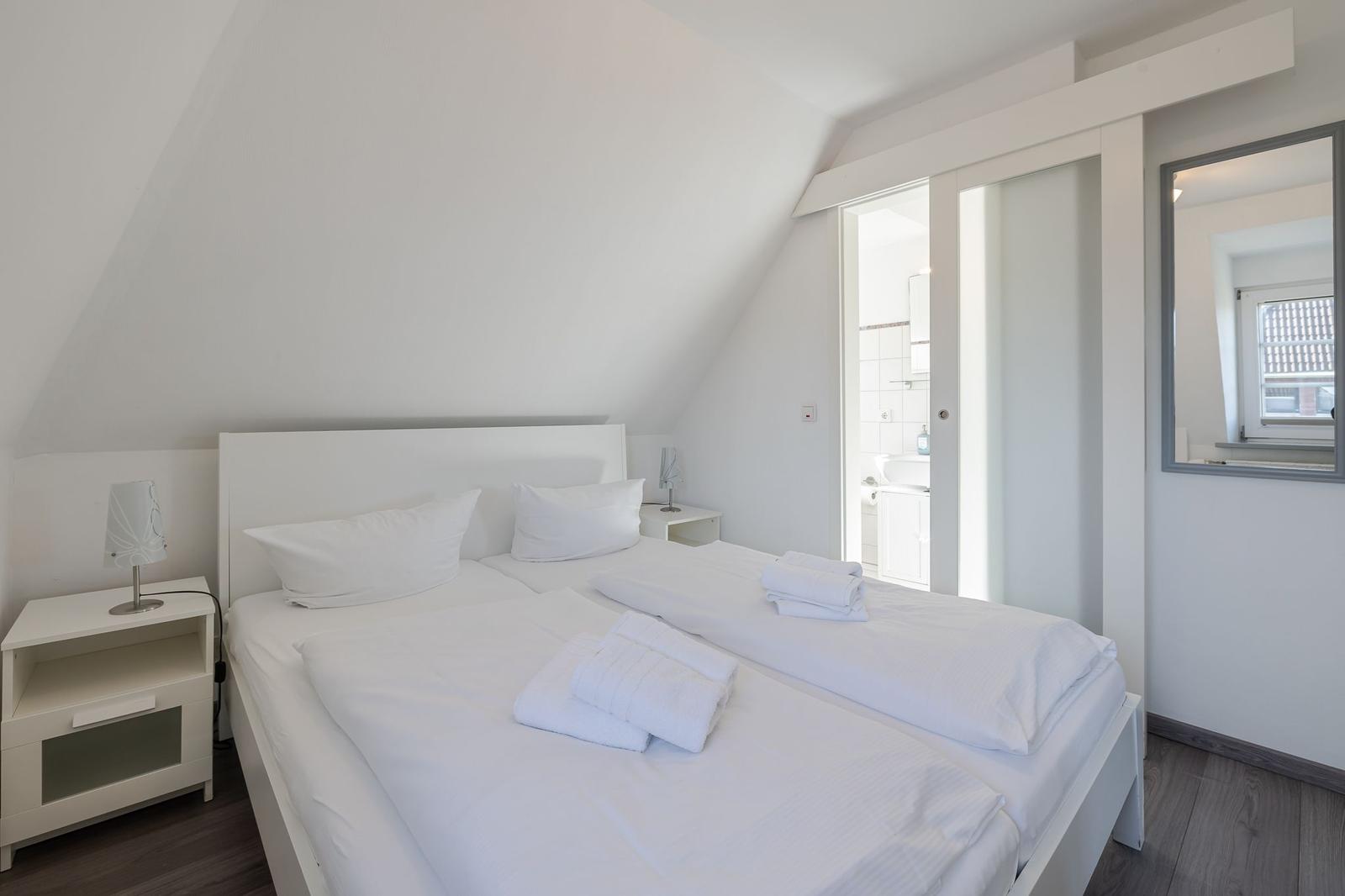 Schlafzimmer mit Doppelbett, Nachttisch und Bad im Hintergrund.