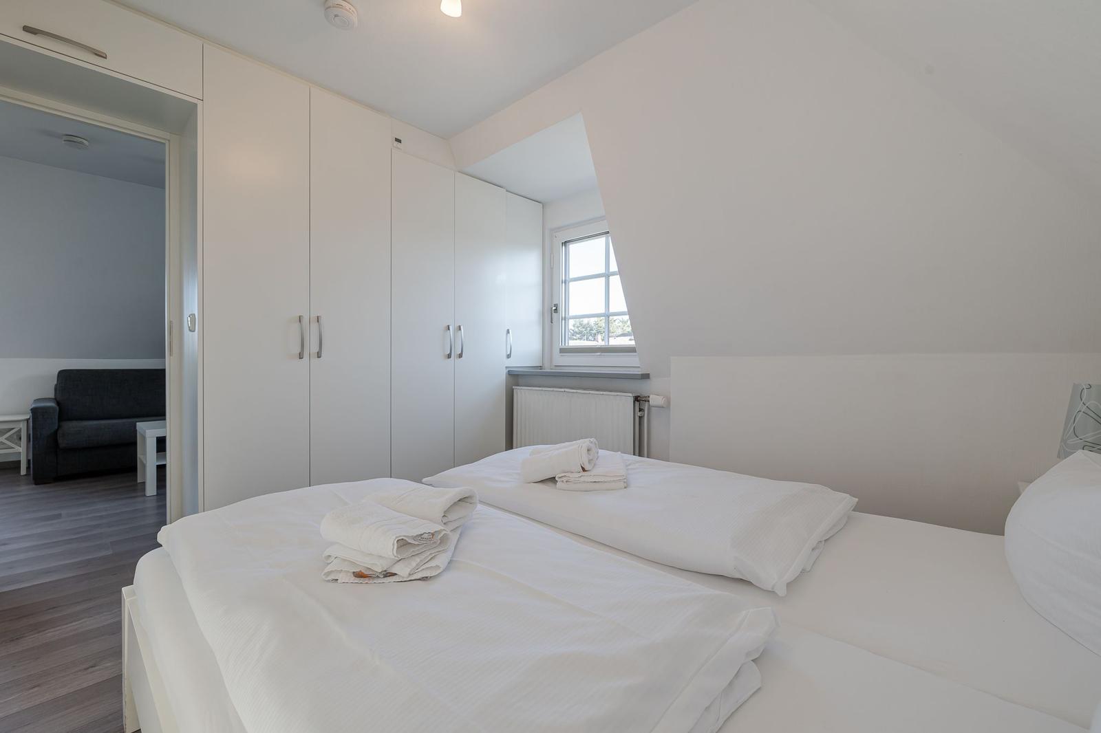 Schlafzimmer mit Doppelbett, weißen Wänden und integriertem Schrank. Durchgang zur Wohnfläche.