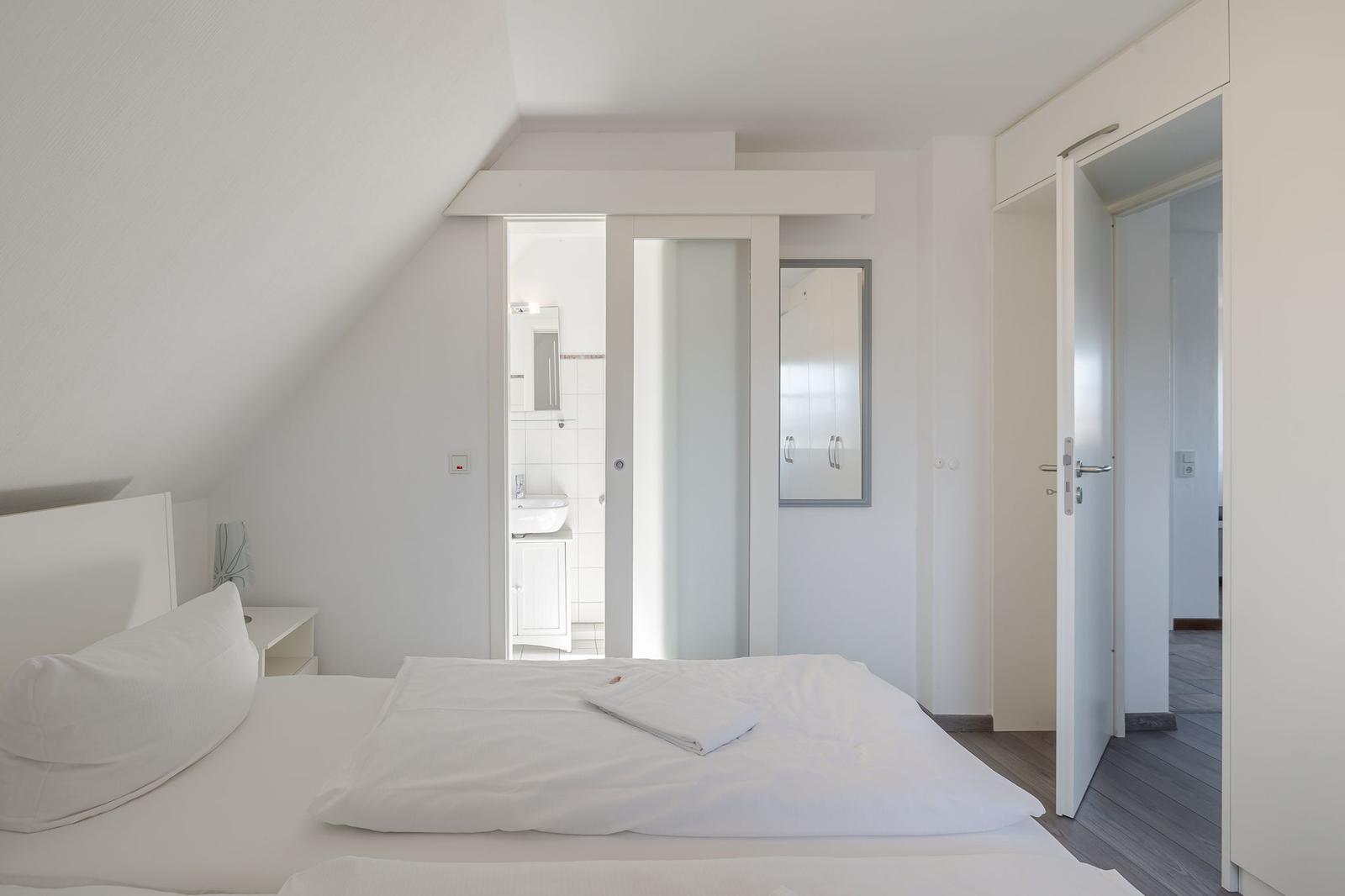 Schlafzimmer mit Dachschräge, Bett, Bad und Tür zum Flur.