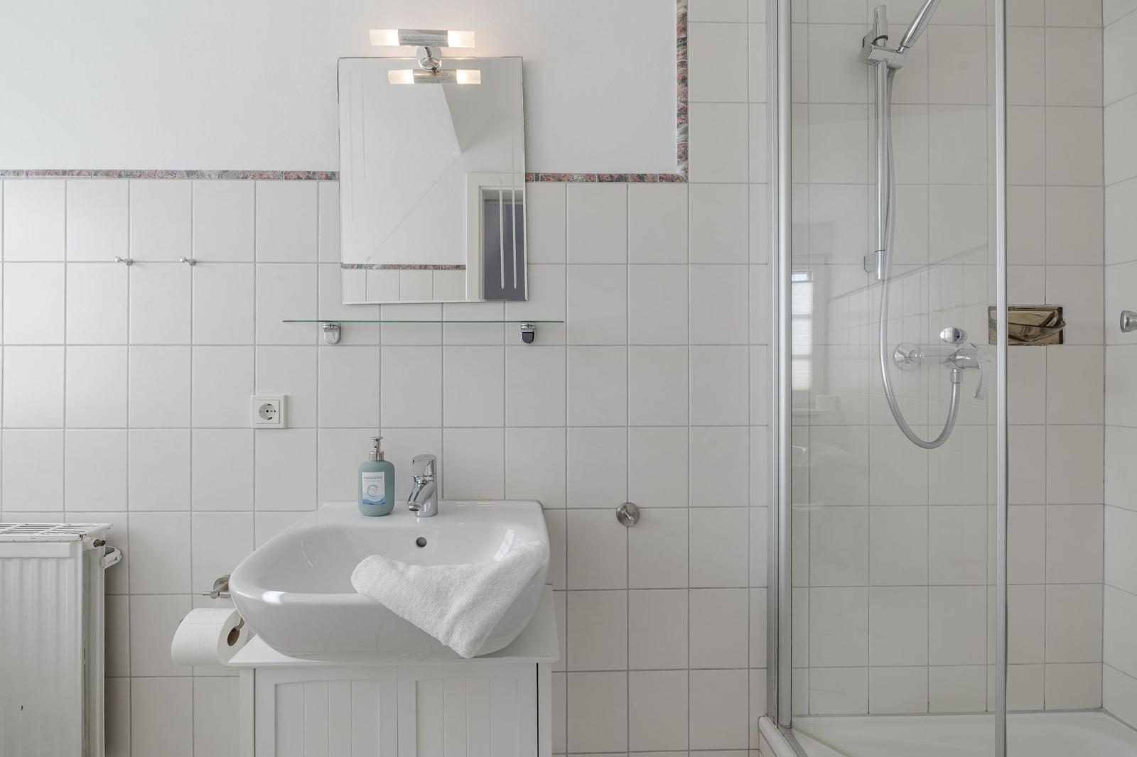Badezimmer mit Dusche, Waschbecken und Spiegel.