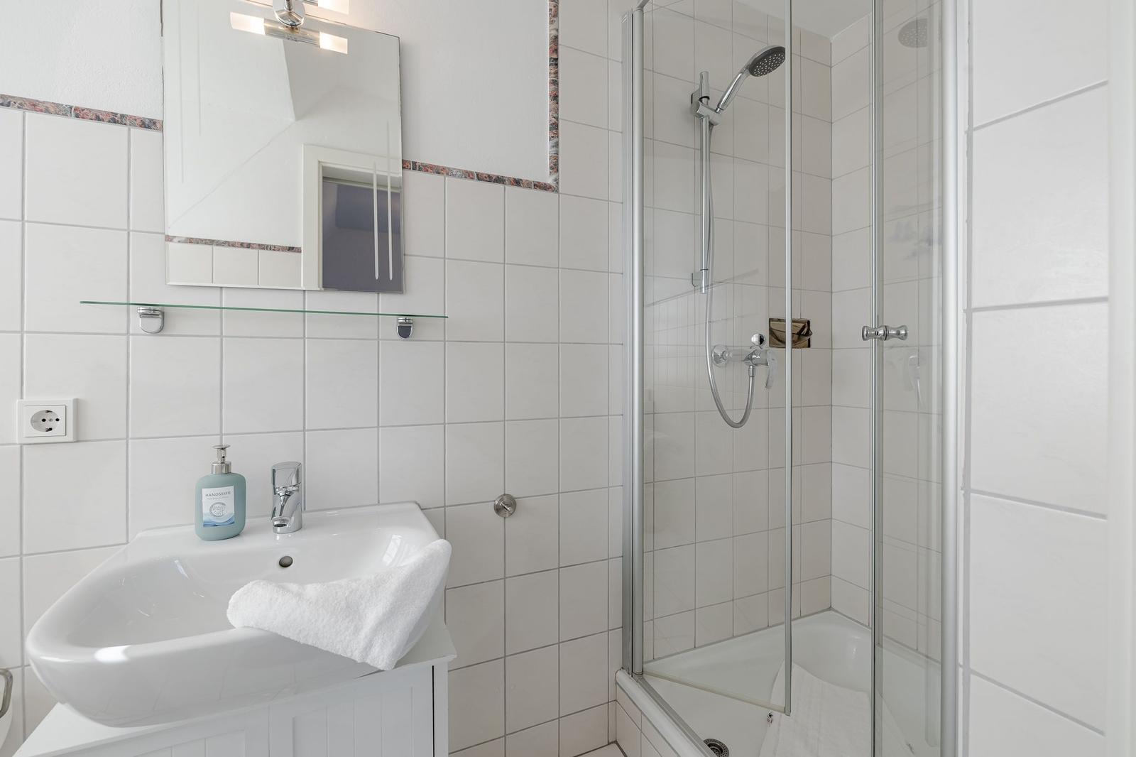 Badezimmer mit Dusche, Waschbecken und Spiegel.