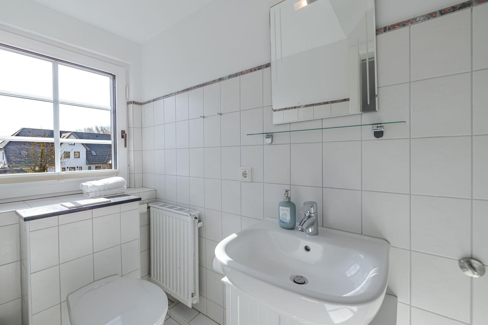 Badezimmer mit Waschbecken, Spiegel und Fenster mit Blick auf Häuser.