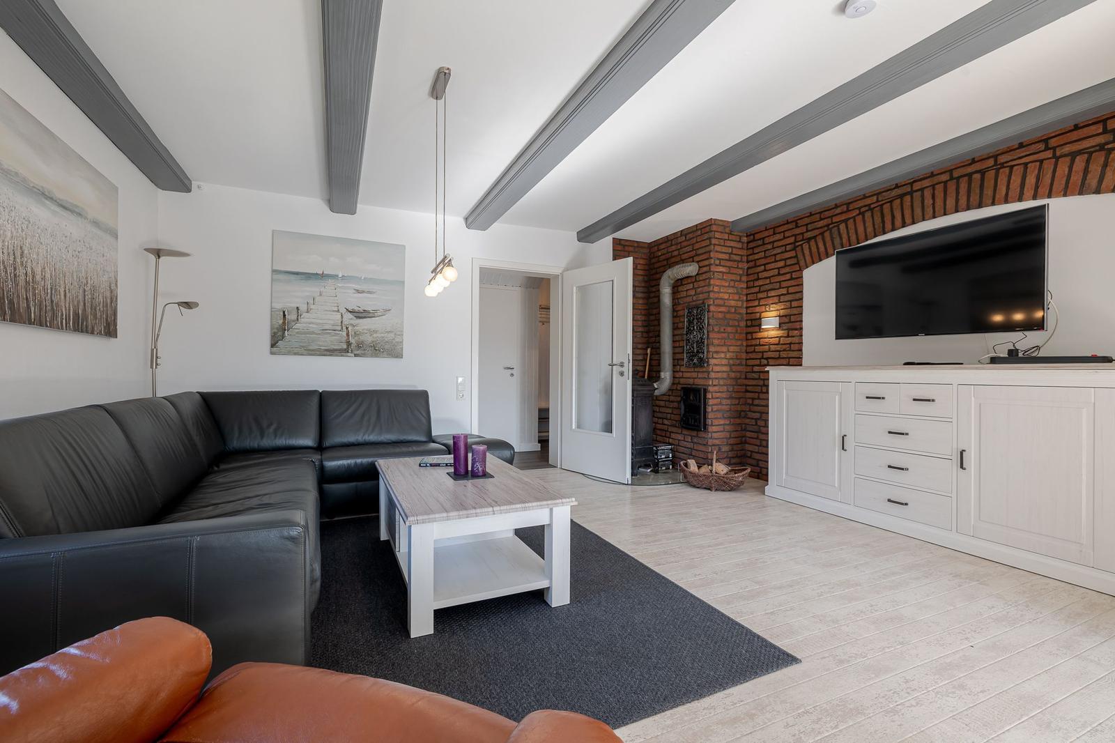 Wohnzimmer mit Ledersofa, Holztisch und Fernseher an der Wand.