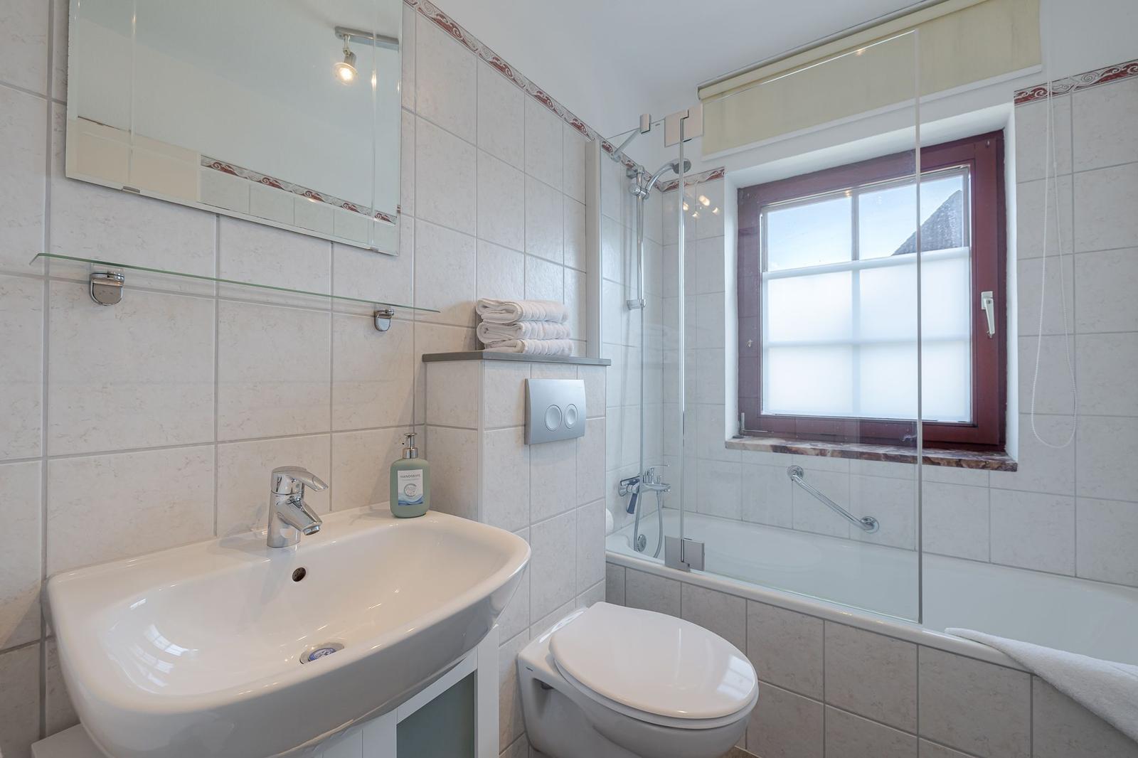 Badezimmer mit Dusche, Waschbecken und Toilette. Fenster mit Rollladen.