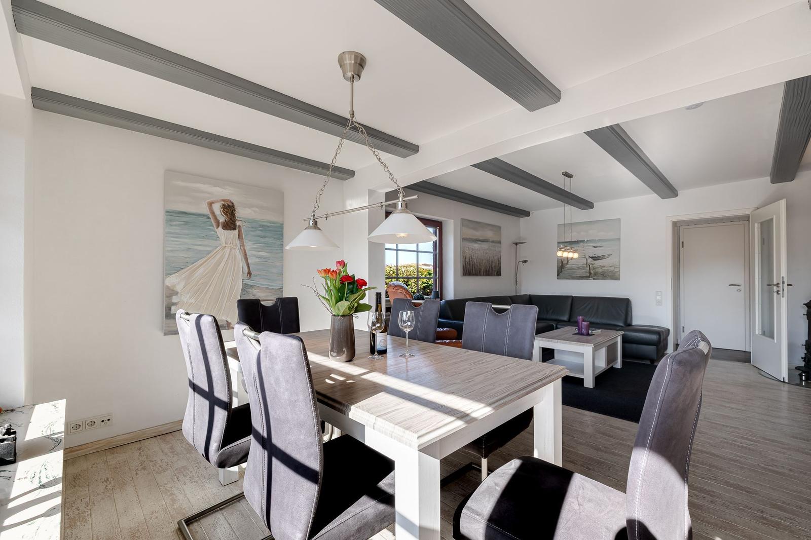 Esszimmer mit Tisch, Stühlen und Wandbildern. Wohnbereich mit Sofa und Couchtisch.