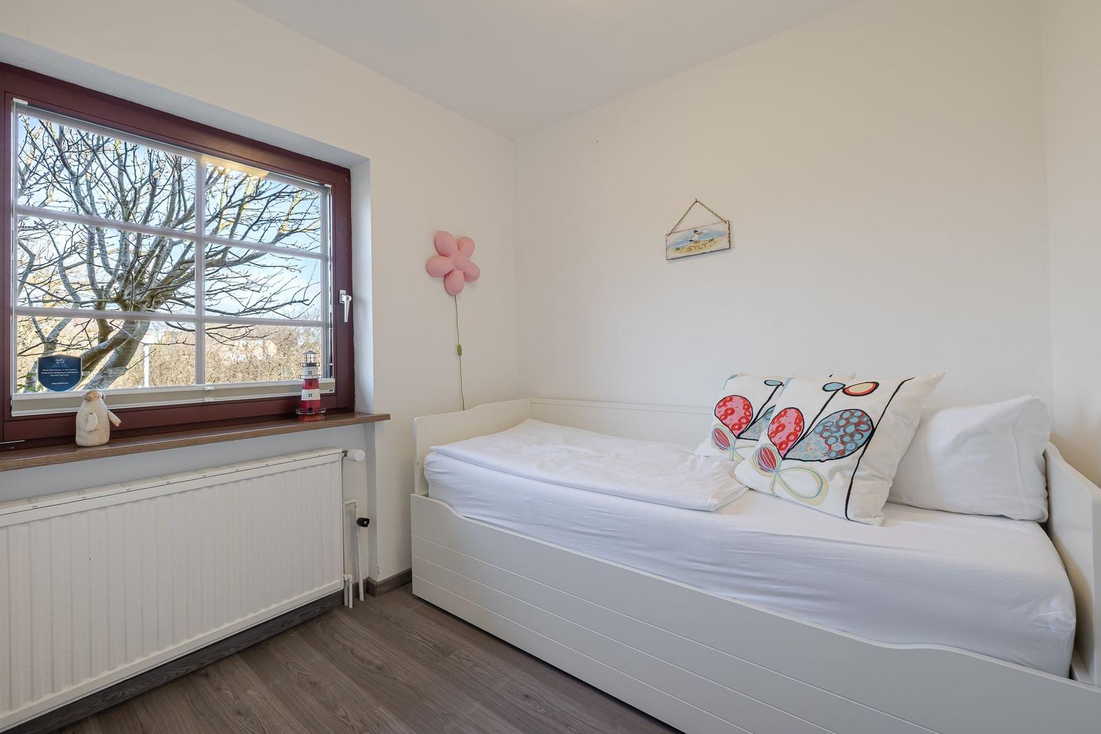 Schlafzimmer mit weißem Bett, Fenster und Wanddekoration.