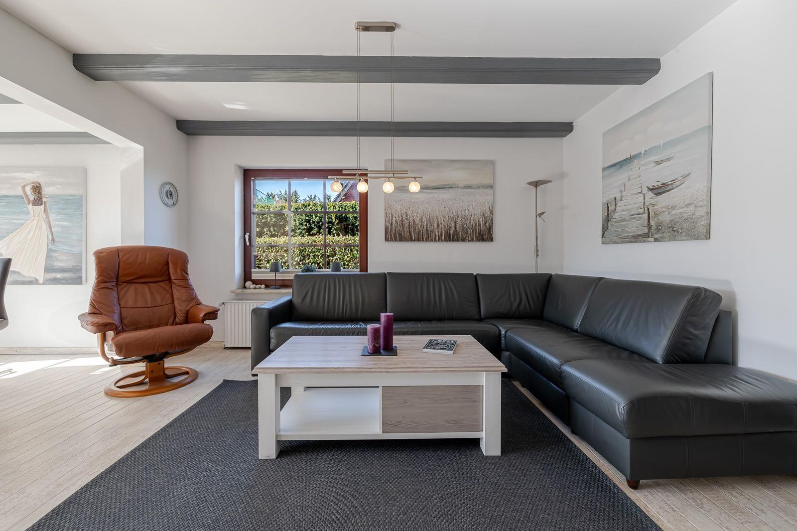 Wohnzimmer mit schwarzer Couch, brauner Sessel und Holztisch.