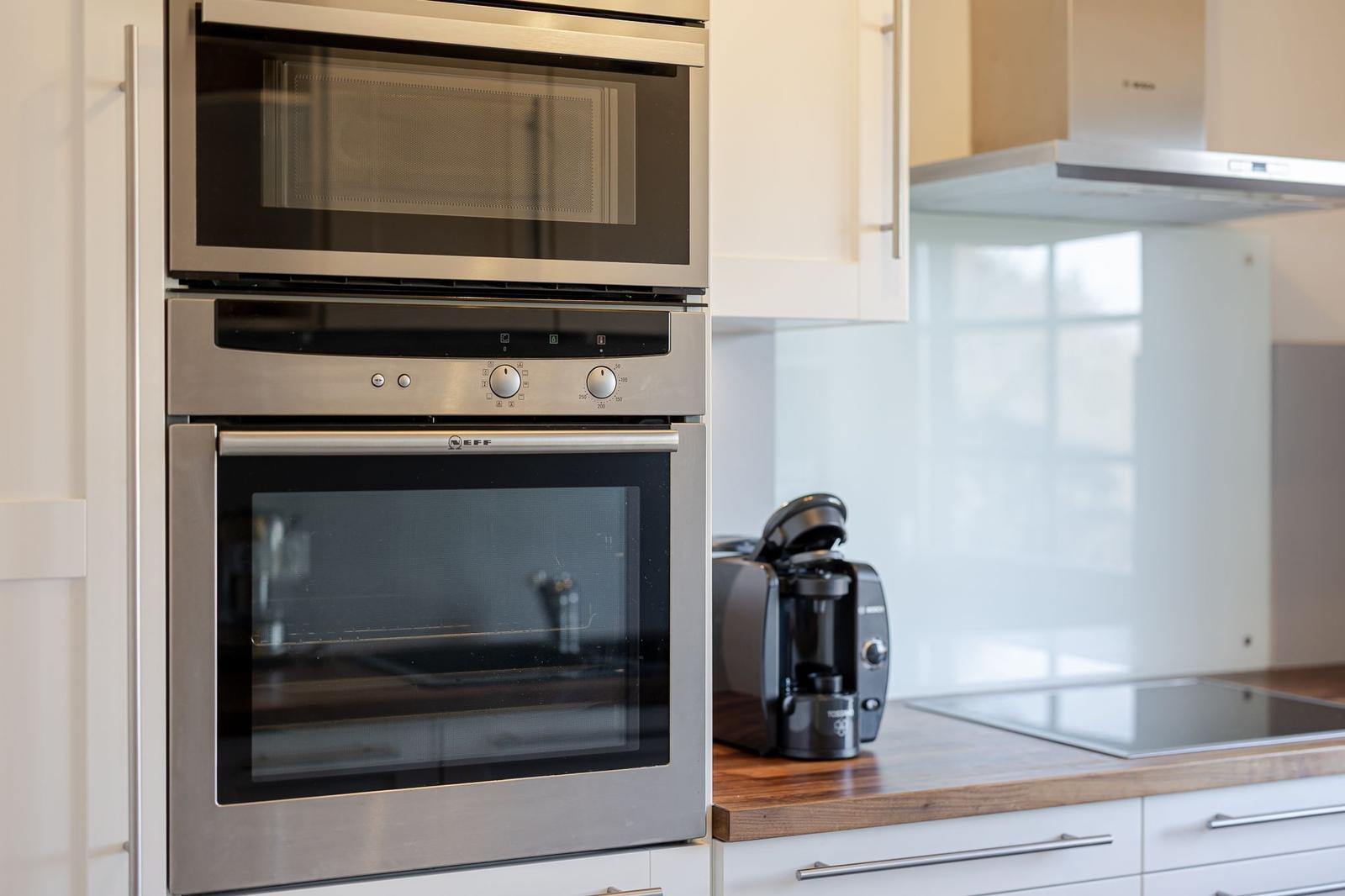 Küche mit eingebauter Mikrowelle und Backofen sowie Kaffeemaschine und Herdplatte.