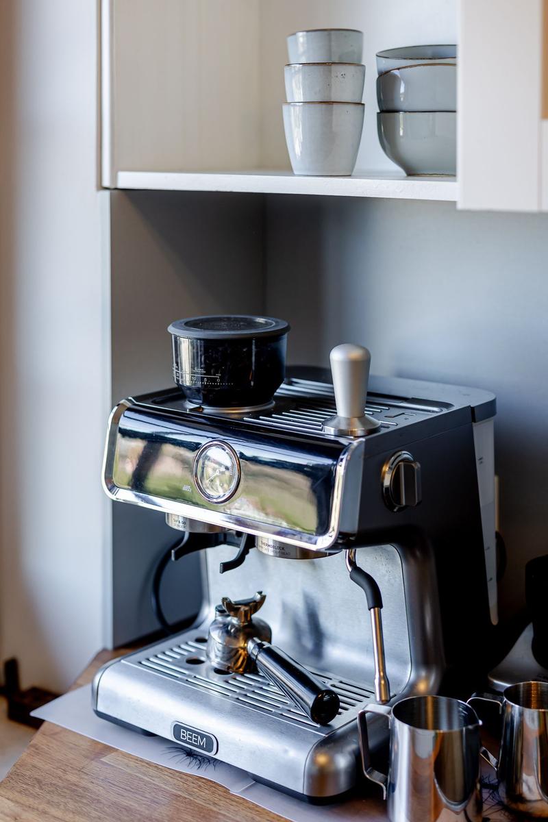 Espresso-Maschine mit Milchkanne und Tassen auf Küchenregal.