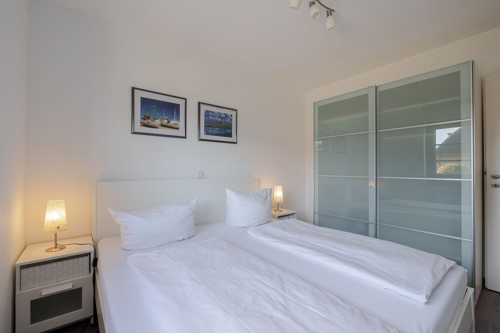 Schlafzimmer mit Doppelbett, Nachttischen und Schwebetüren.