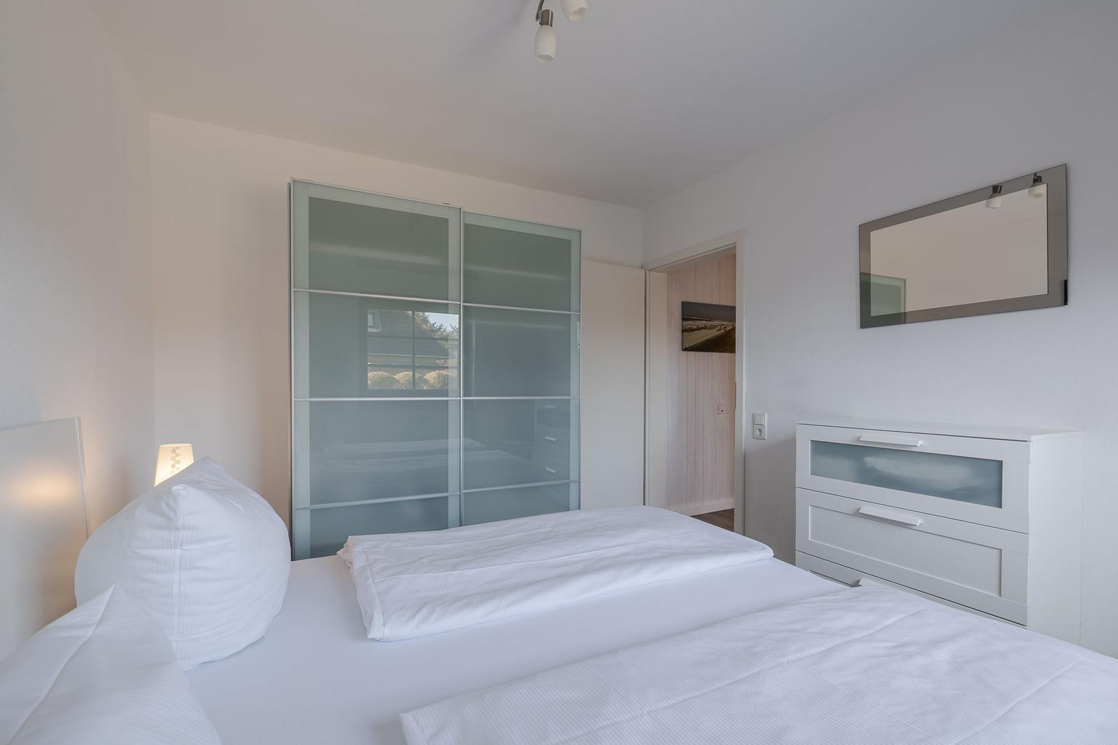 Schlafzimmer mit weißem Bett, Schrank und Spiegelschrank