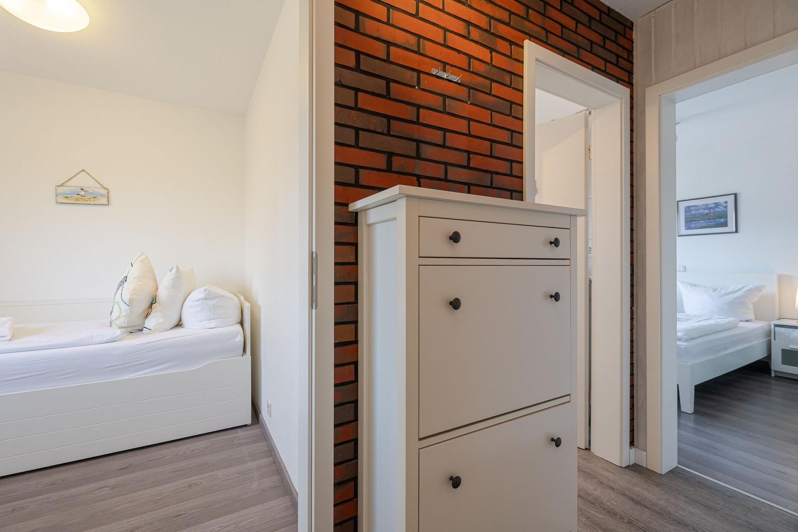 Zimmer mit weißem Bett und Backsteinwand. Schrank und Türen zu weiteren Räumen.
