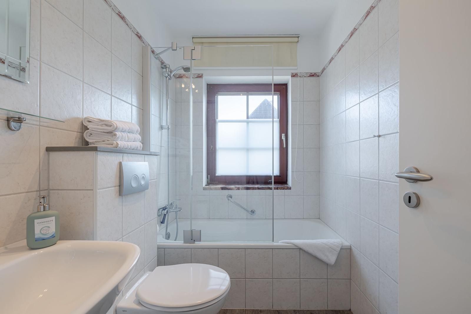 Badezimmer mit Badewanne, Dusche und Fenster. Handtuch und Seife bereit.