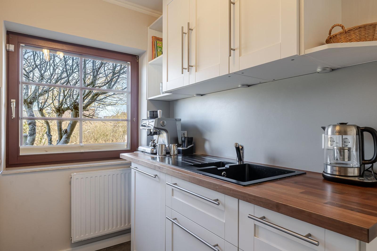 Küche mit Holzoberfläche, schwarzer Spüle und Fensterblick auf Bäume