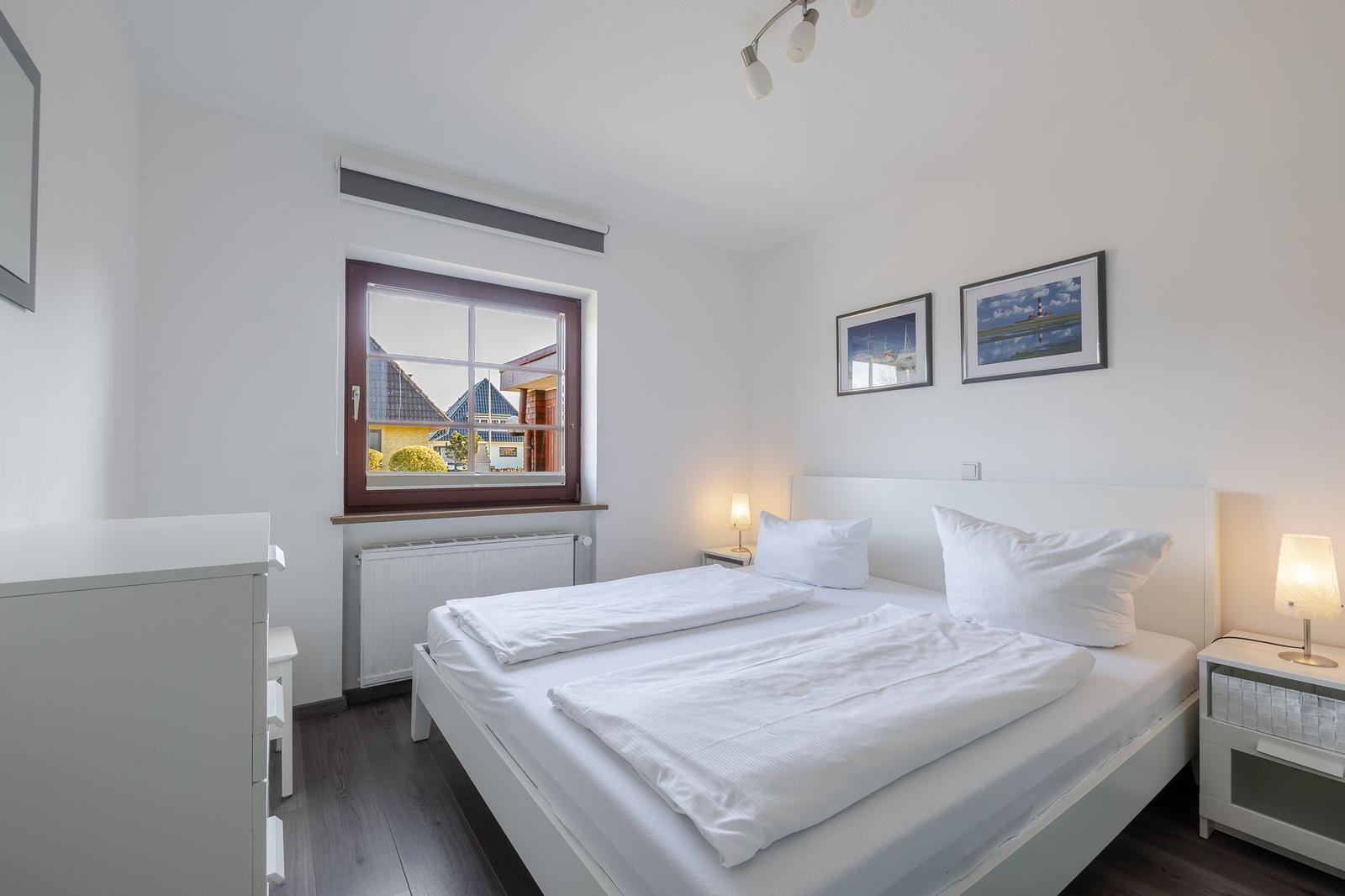 Schlafzimmer mit weißem Bett, Fenster und Nachttischen.