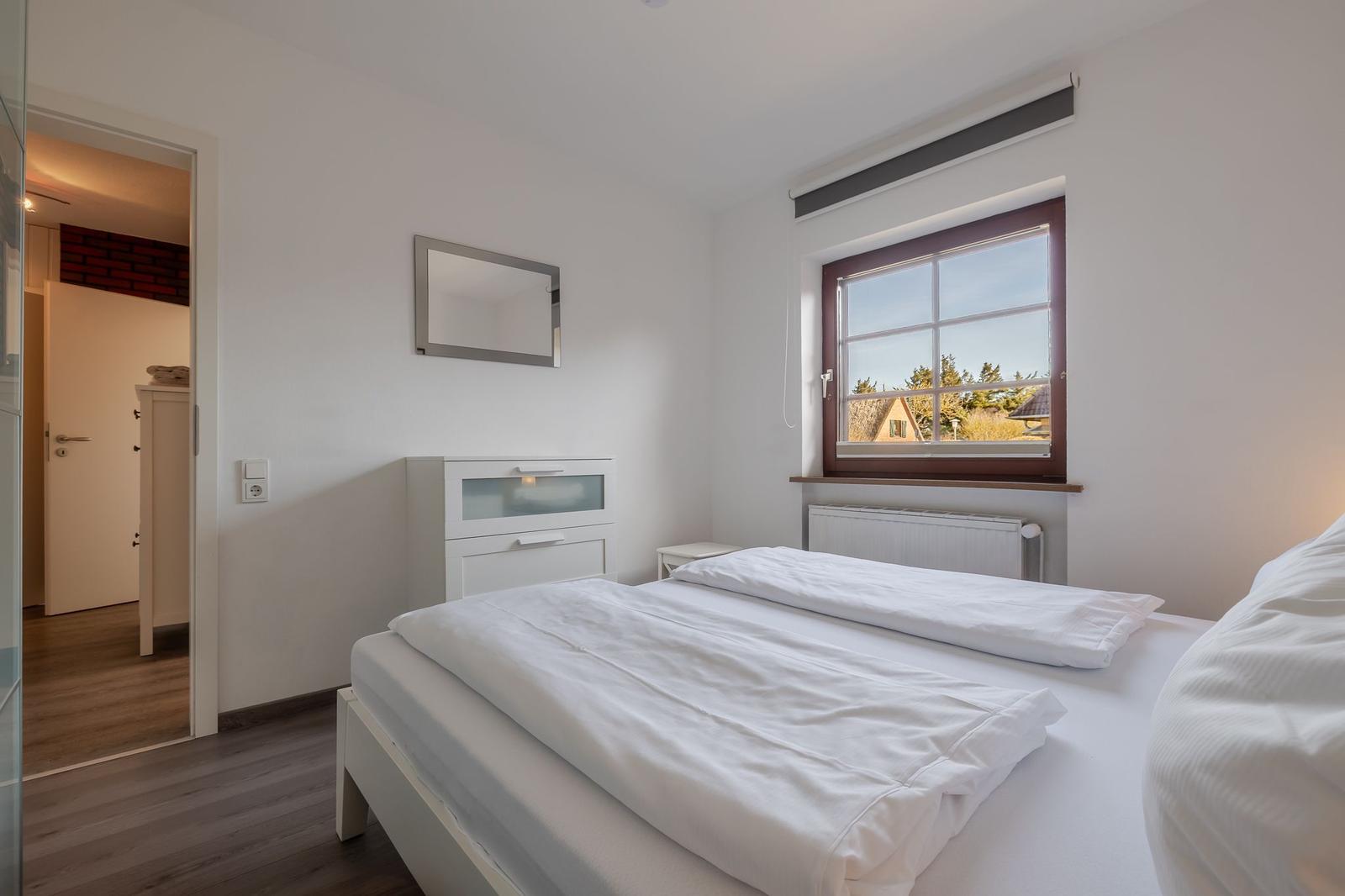 Schlafzimmer mit Doppelbett, Fenster und Spiegel an der Wand.