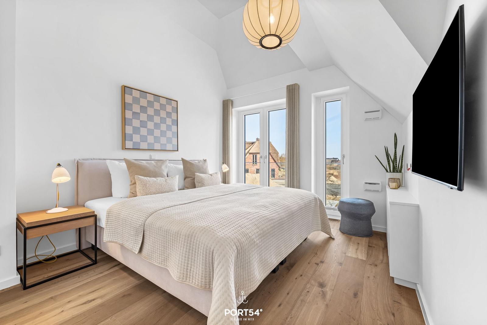 Schlafzimmer mit Bett, TV und Fensterblick auf Außenbereich.