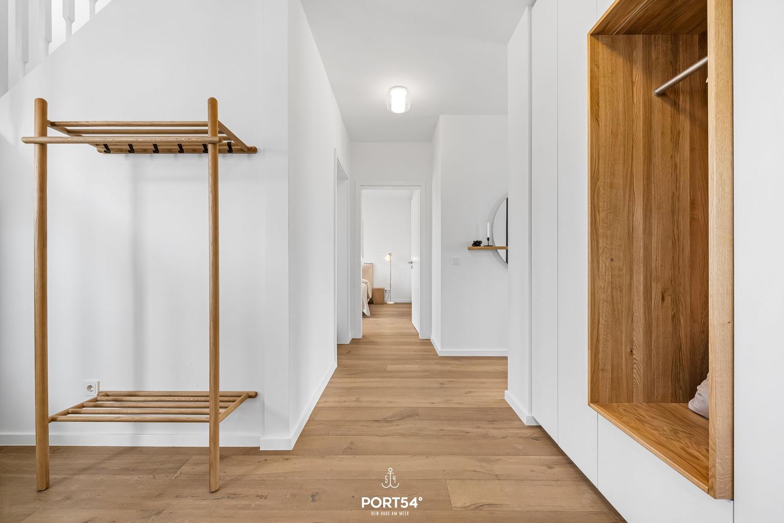 Flur mit Holzregal, Kleiderständer und integriertem Schrank. Holzfußboden und weiße Wände.