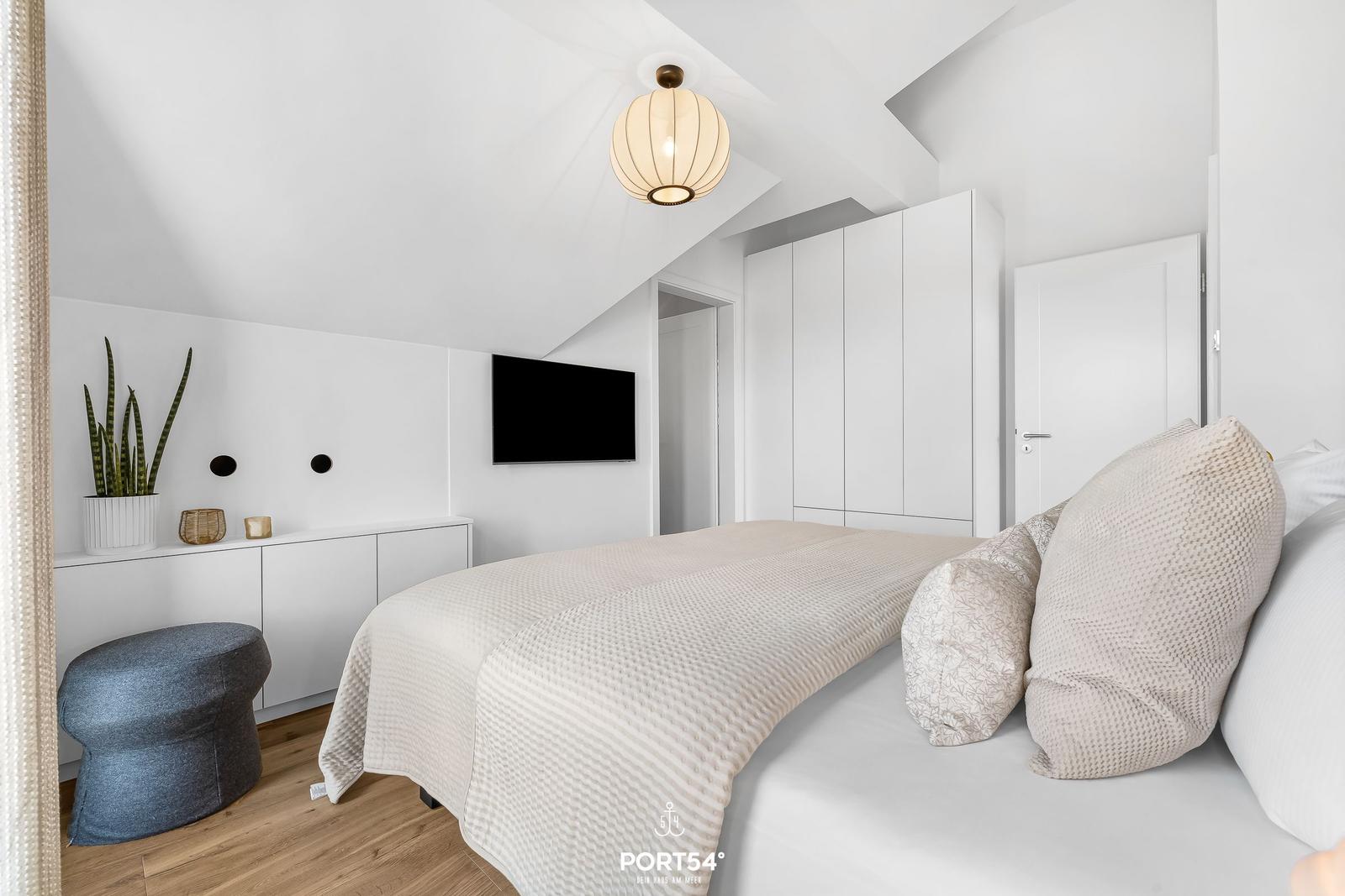 Schlafzimmer mit Bett, Schrank und Fernseher an der Wand.