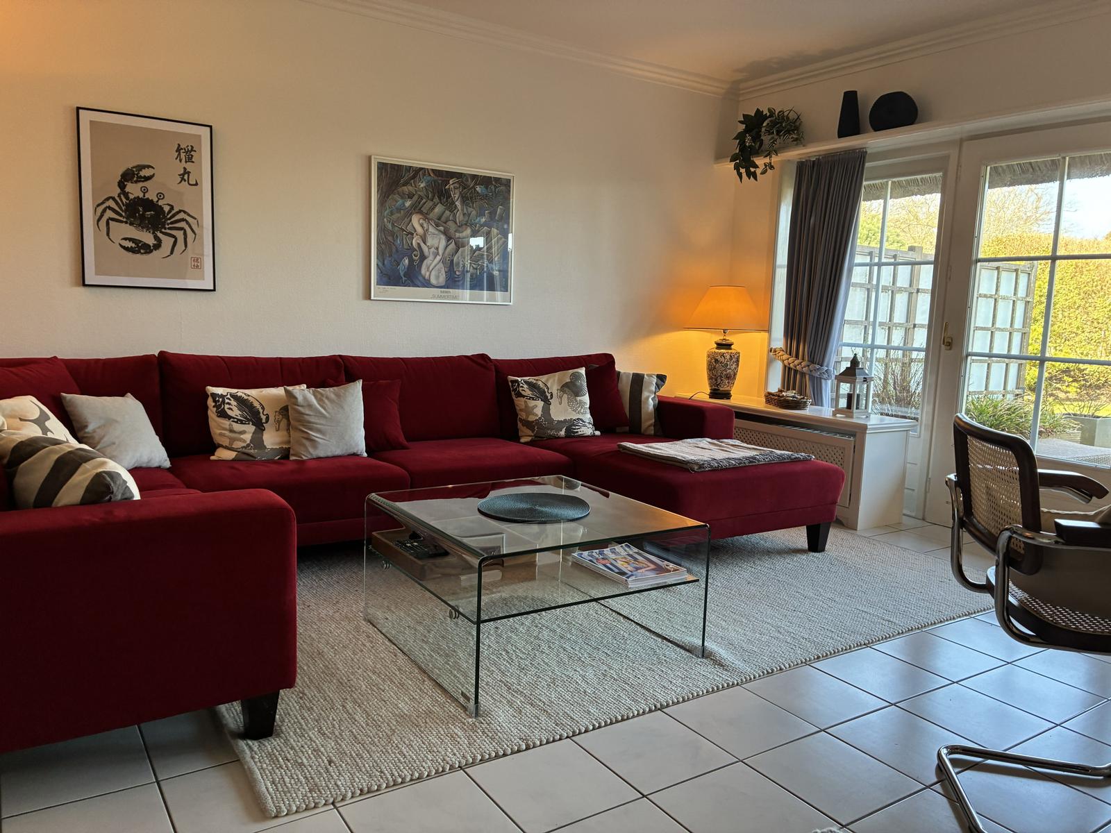 Ein Wohnzimmer mit rotem Sofa, Glas-Tisch und Blick auf einen Garten.