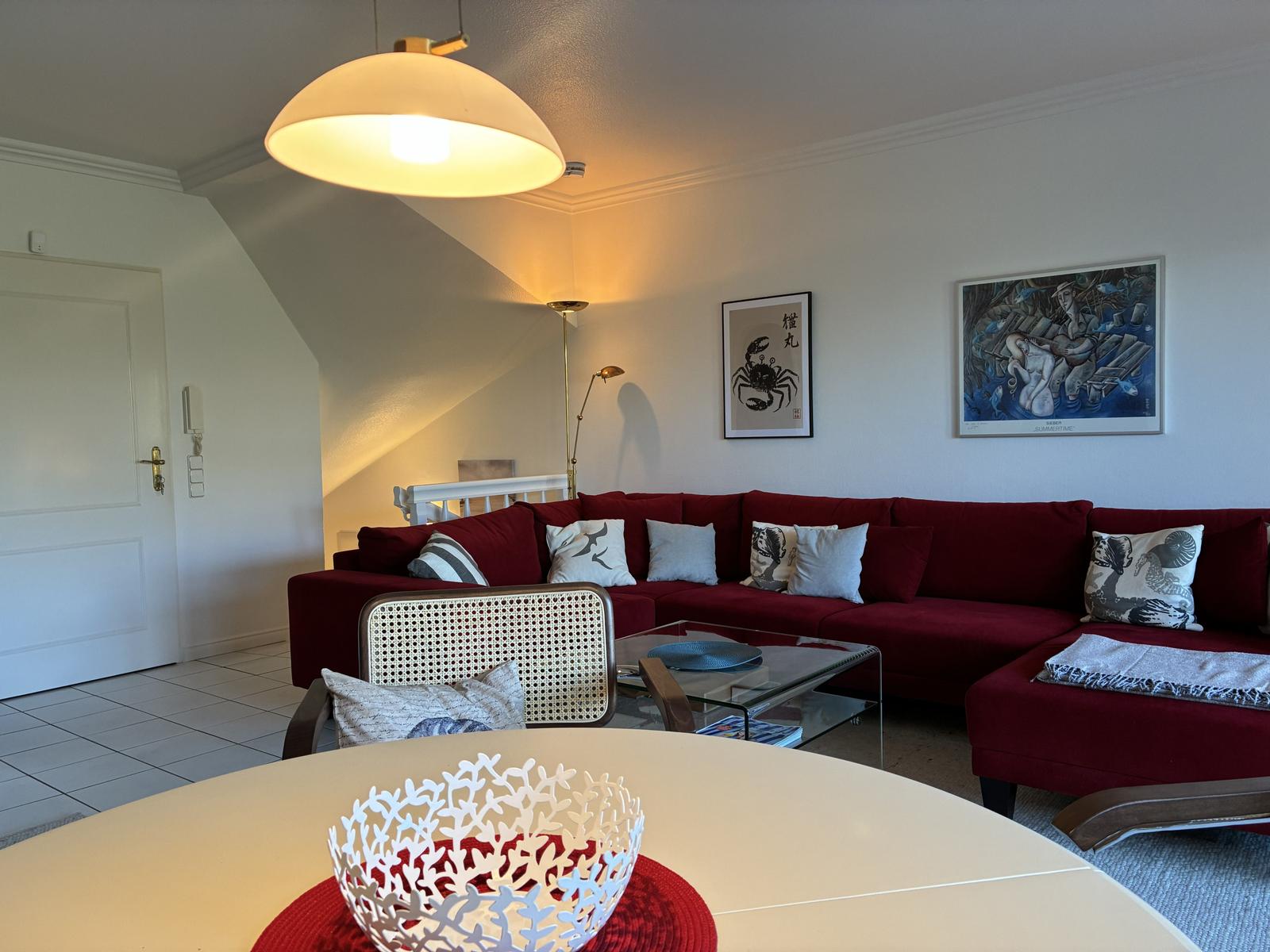 Ein Wohnzimmer mit rotem Sofa, Glas-Tisch und Wandbildern.