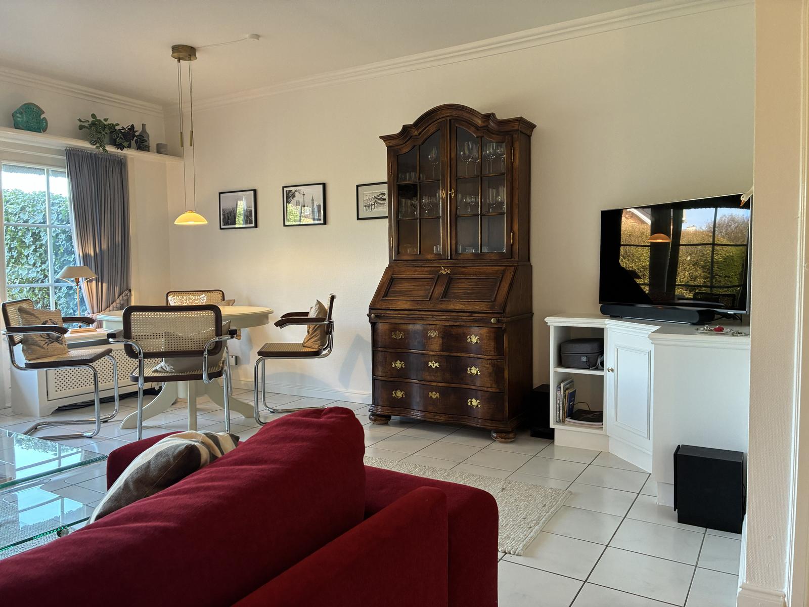 Wohn- und Essbereich mit rotem Sofa, Esstisch und antikem Schrank.