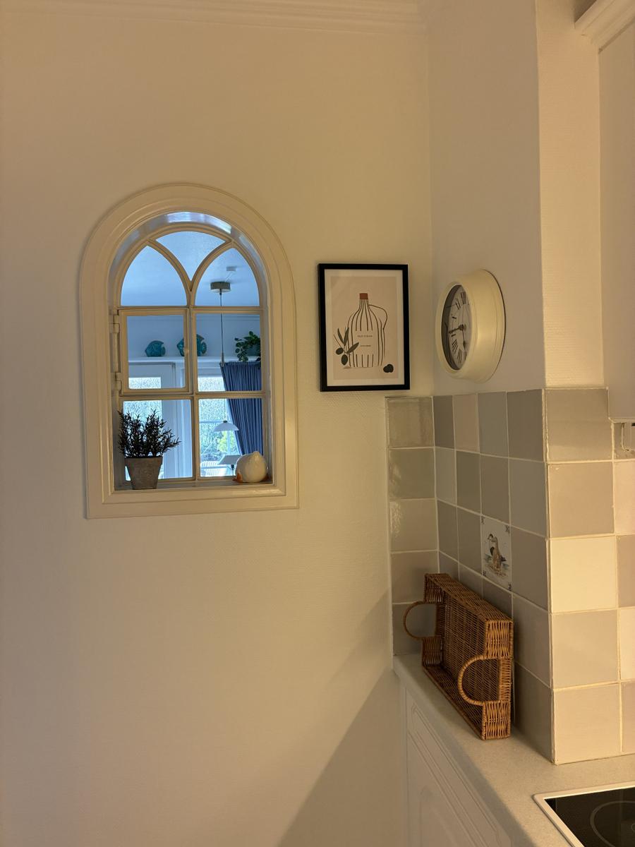 Küchenwand mit Fliesen, Wanduhr, Bild und Bogenfenster mit Pflanze.
