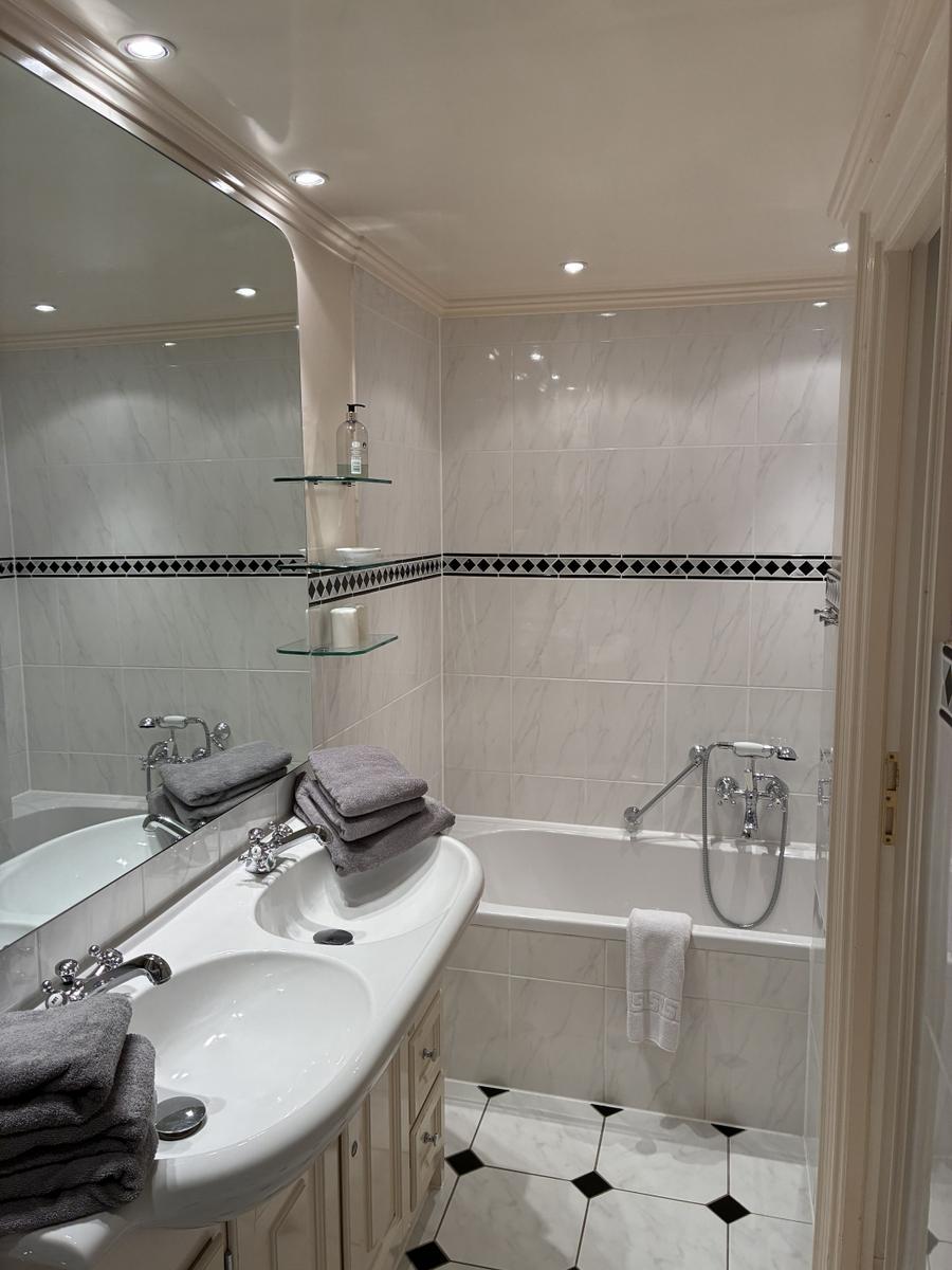 Badezimmer mit Badewanne, Waschbecken und Spiegel. Fliesen und Handtücher sind sichtbar.