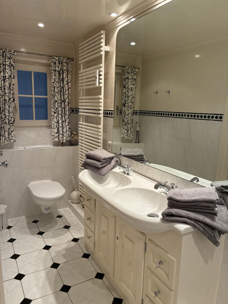 Badezimmer mit Waschbecken, Spiegel, Toilette und Fenster mit Vorhängen.