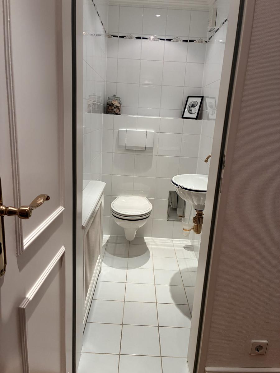 Badezimmer mit Toilette, Waschbecken und Dusche. Weiße Fliesen und goldene Wasserhähne.
