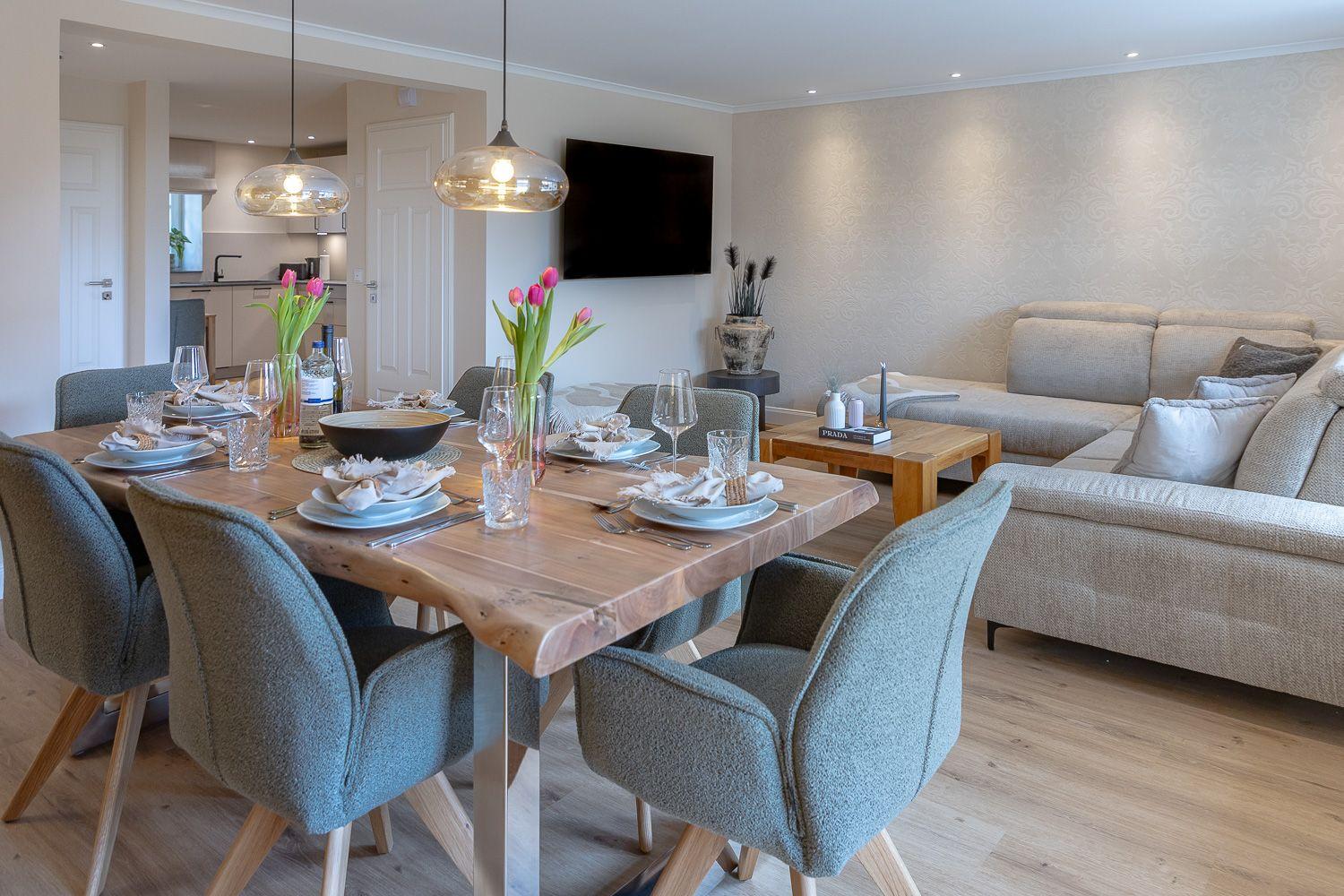 Esszimmer mit Esstisch und Stühlen. Wohnzimmer mit Sofa und Fernseher. Holzboden und Pendelleuchten.