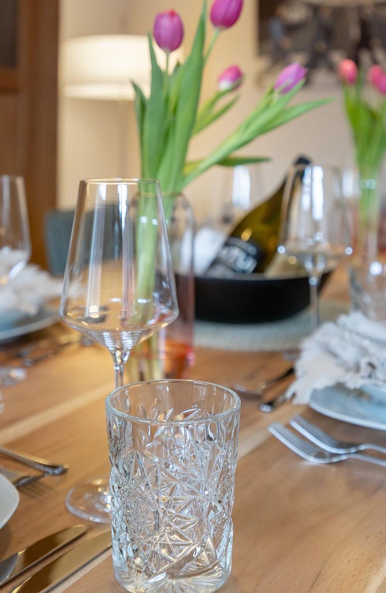 Gestellte Tischdekoration mit Tulpen, Gläsern und Geschirr auf Holztisch.