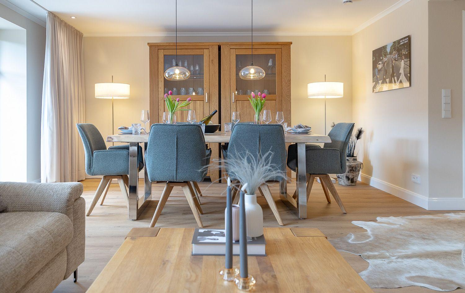 Esszimmer mit Holztisch, blauen Stühlen und Glaswand-Schrank. Holzboden und Wandbild.