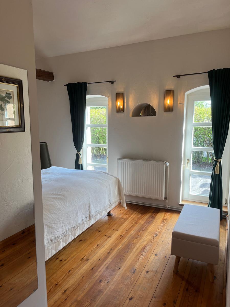 Schlafzimmer mit Holzboden, Bett, zwei Fenster und Sitzbank.