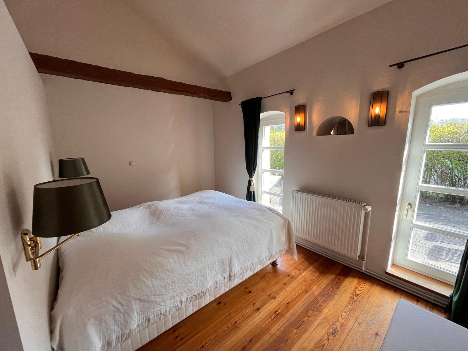 Schlafzimmer mit Holzboden, Bett, Fenster und Wandleuchten.