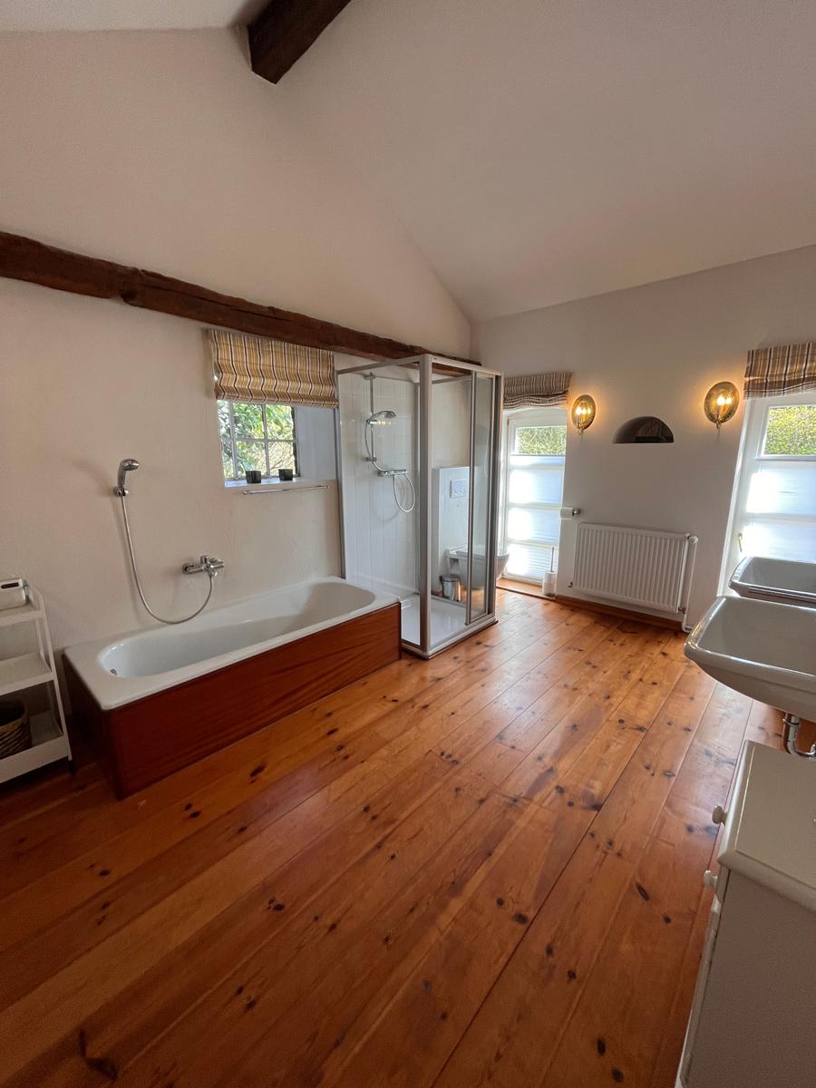 Badezimmer mit Badewanne, Dusche und Holzboden.