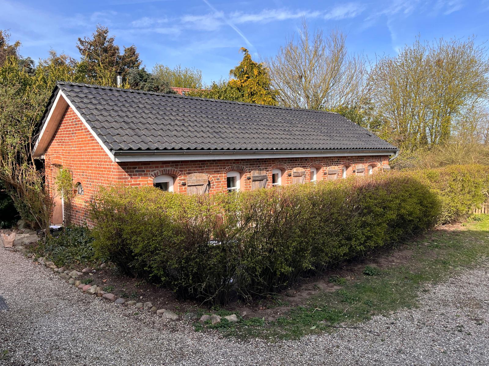 Rotes Backsteinhaus mit Dach und Hecken. Garten mit Kiesweg.