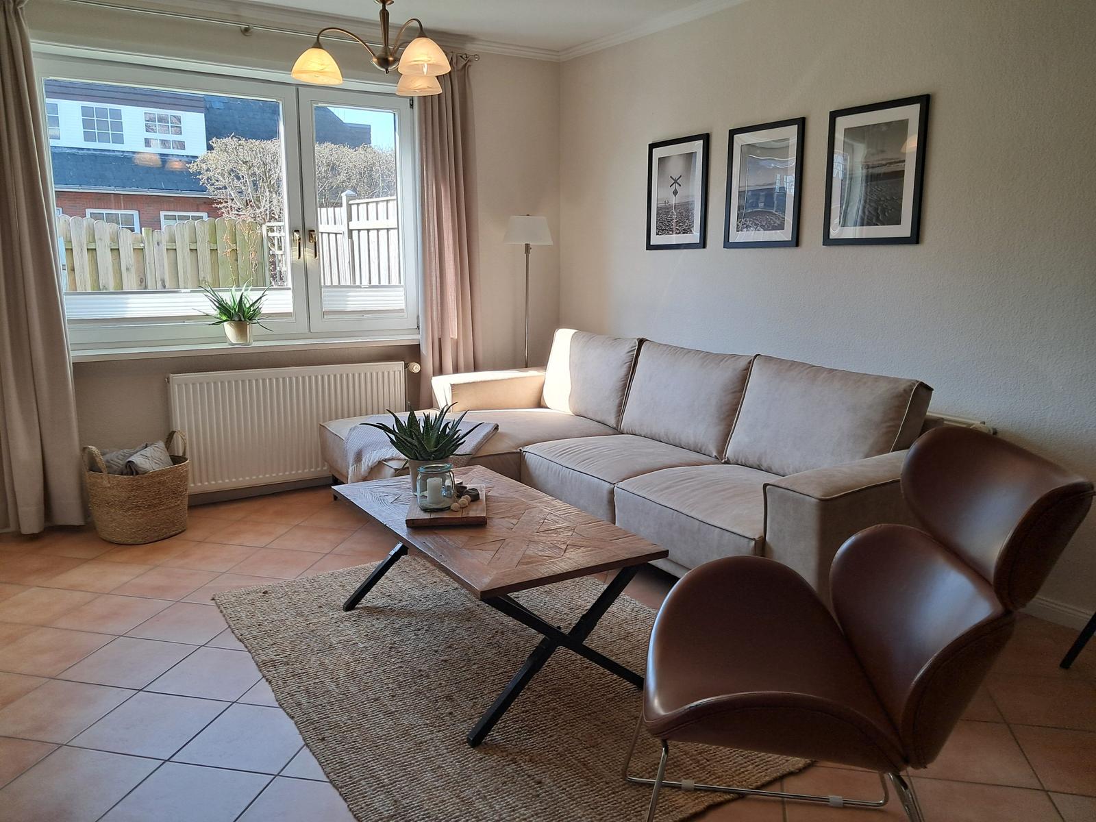 Wohnzimmer mit Sofa, Stuhl, Tisch und Fenster. Wandbilder und Teppich.