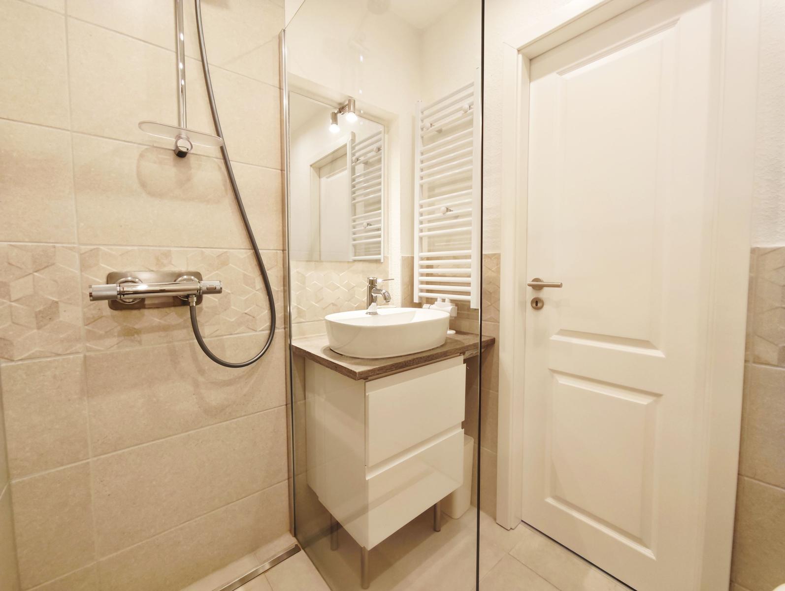 Badezimmer mit Dusche, Waschbecken und Heizkörper