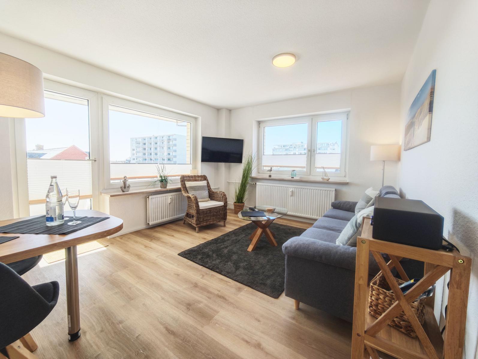 Wohnzimmer mit Sofa, Esstisch und großen Fenstern.