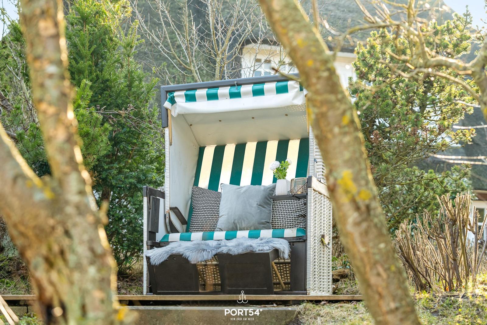 Ein Strandkorb mit grün-weißem Streifenmuster und Kissen im Garten.