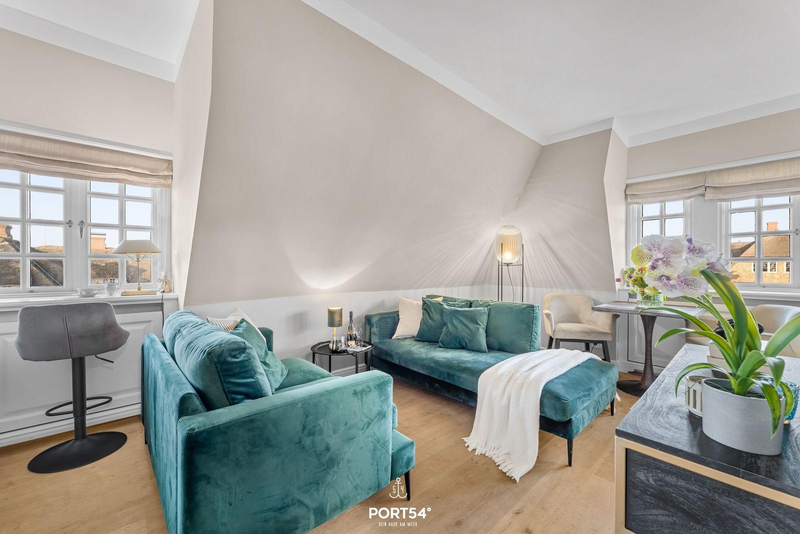 Ein Wohnzimmer mit grünem Sofa, Holzboden und großen Fenstern.