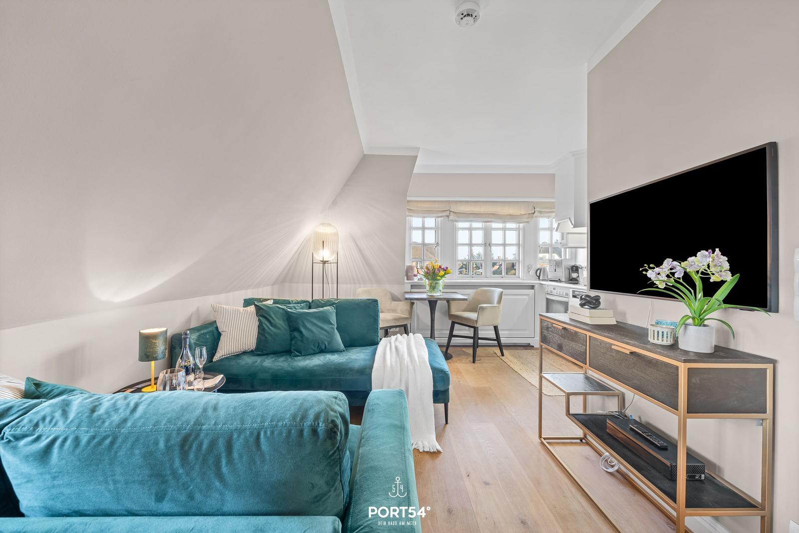 Wohnzimmer mit Sofa, Fernseher und Essbereich. Holzboden und großes Fenster.