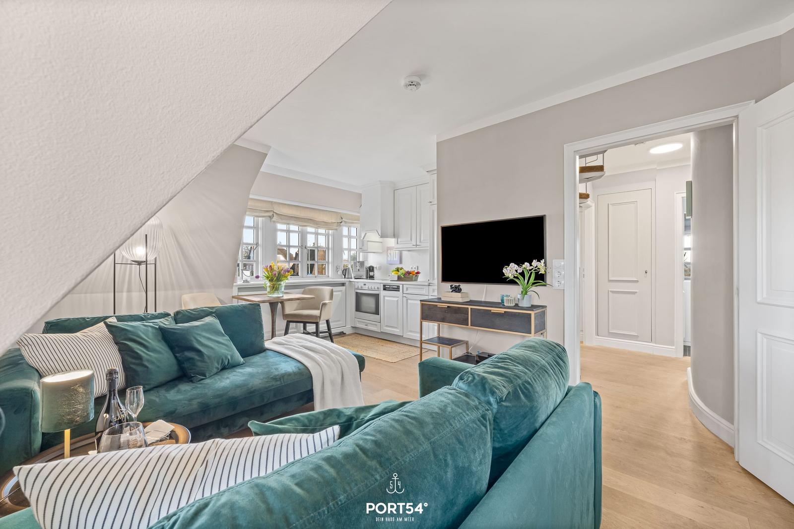 Wohnbereich mit Sofa, Fernseher und Küche im Hintergrund.