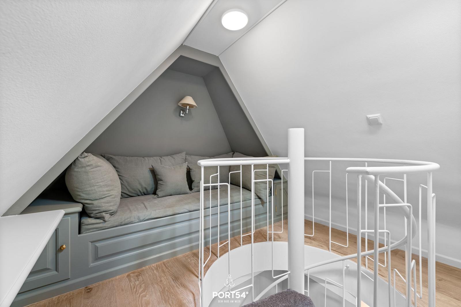 Dachbodenwohnung mit Sitzbank, weiße Wendeltreppe und Holzboden.