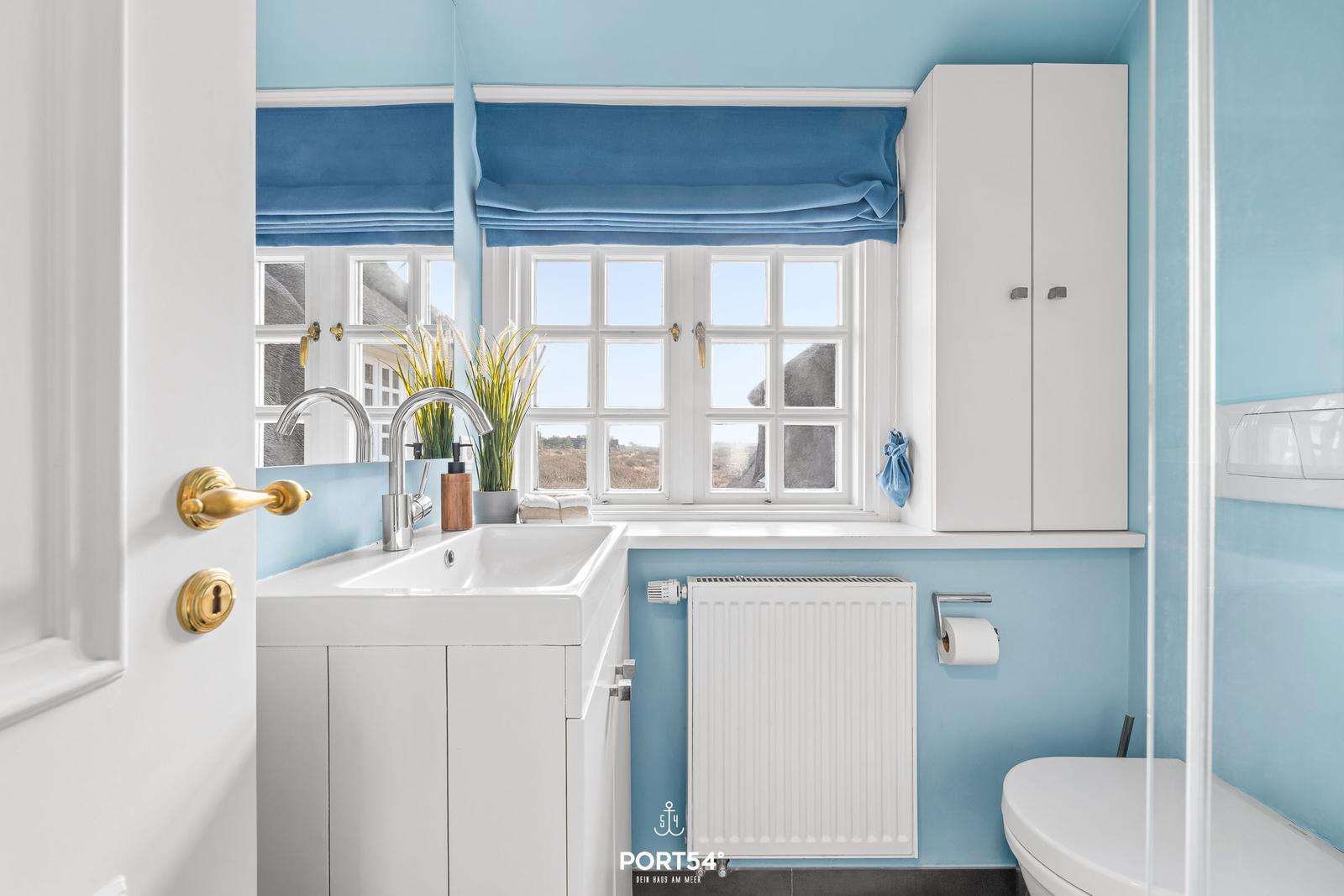 Badezimmer mit blauen Wänden, weißem Waschbecken und Fenster mit blauem Rollladen.