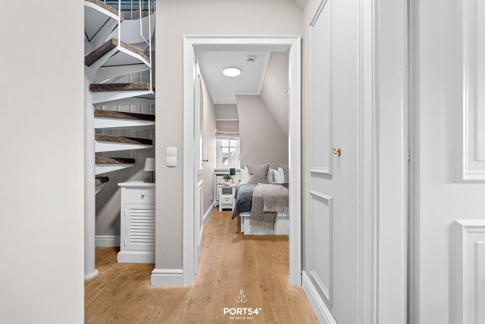 Schlafzimmer mit Bett und Fenster. Nebenher Wendeltreppe und Holzboden.
