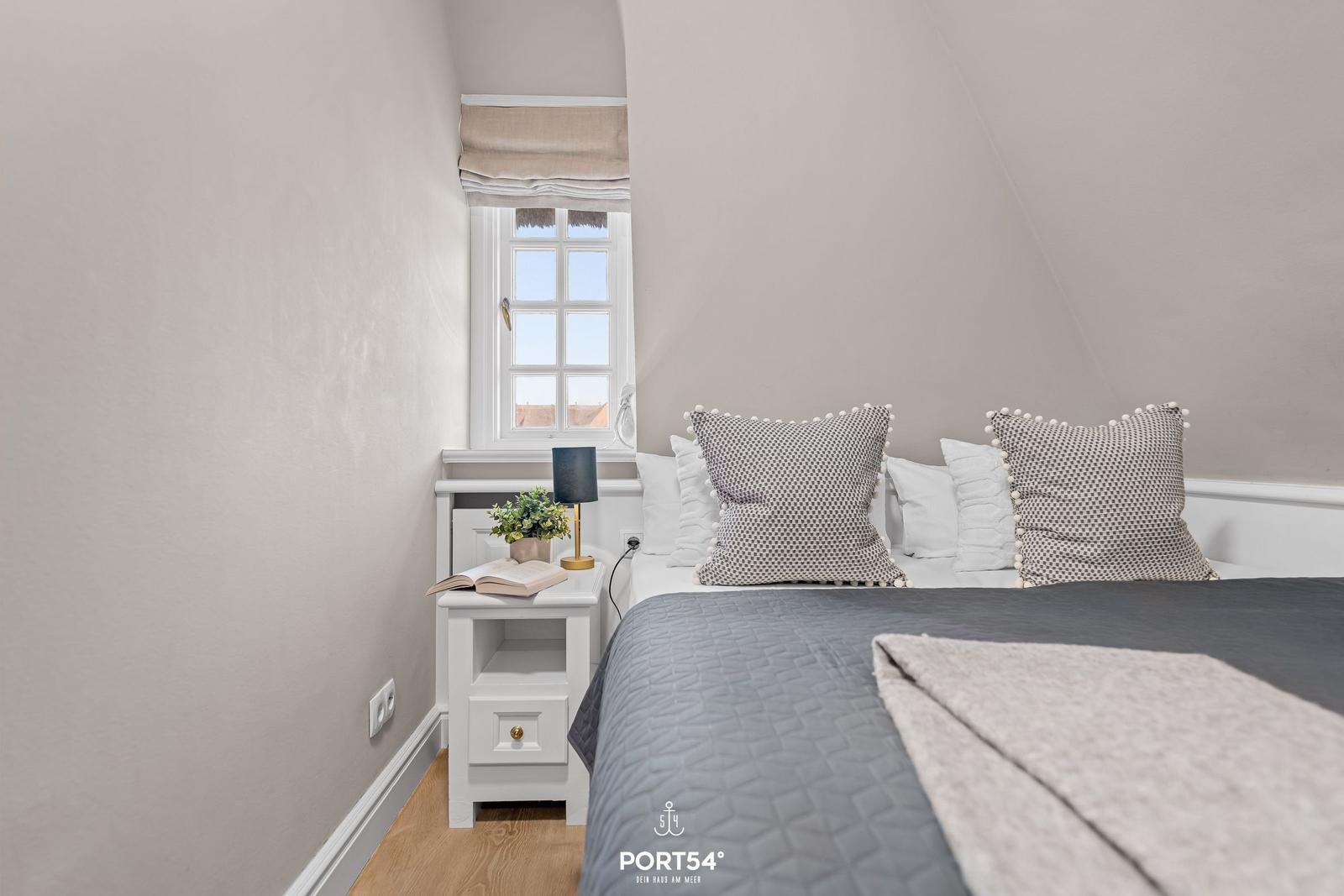 Schlafzimmer mit Dachschrägen, Fenster und Bett mit Kissen.