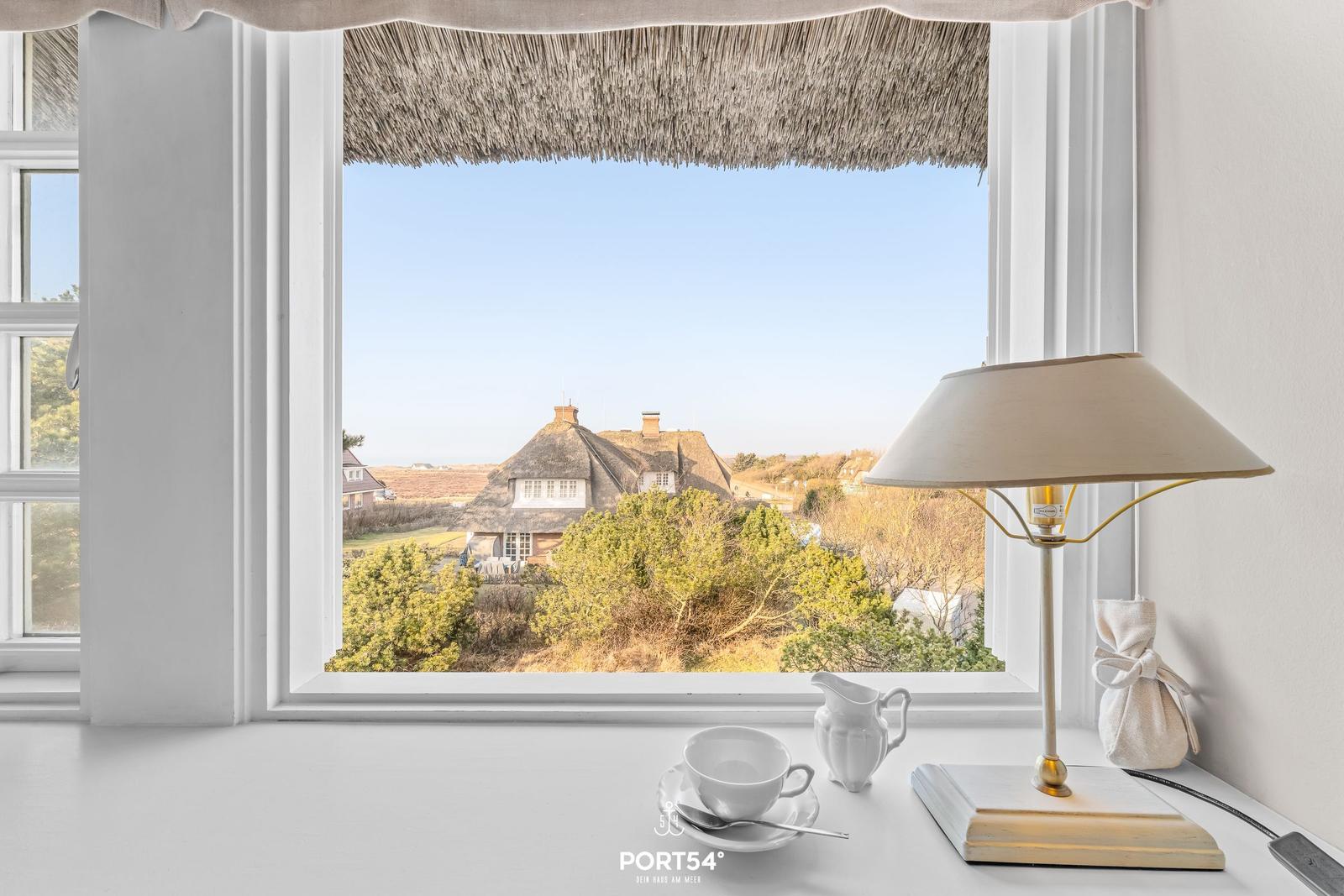 Terasse mit Blick auf strohgedeckte Häuser und Grünflächen.